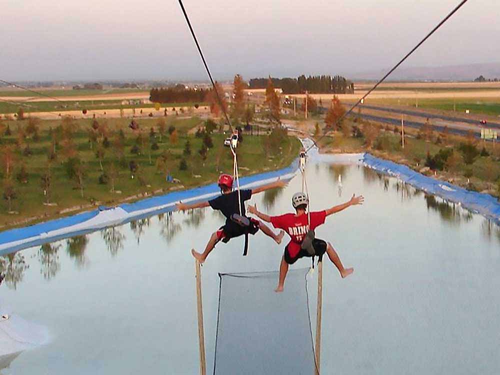 Two kids on a zipline careening toward water.