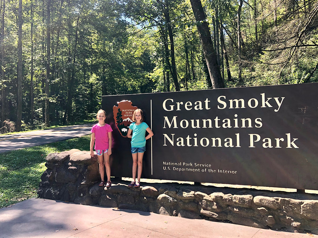 Two kids stand in front of the Great Smoky Mountain National Park entrance sign