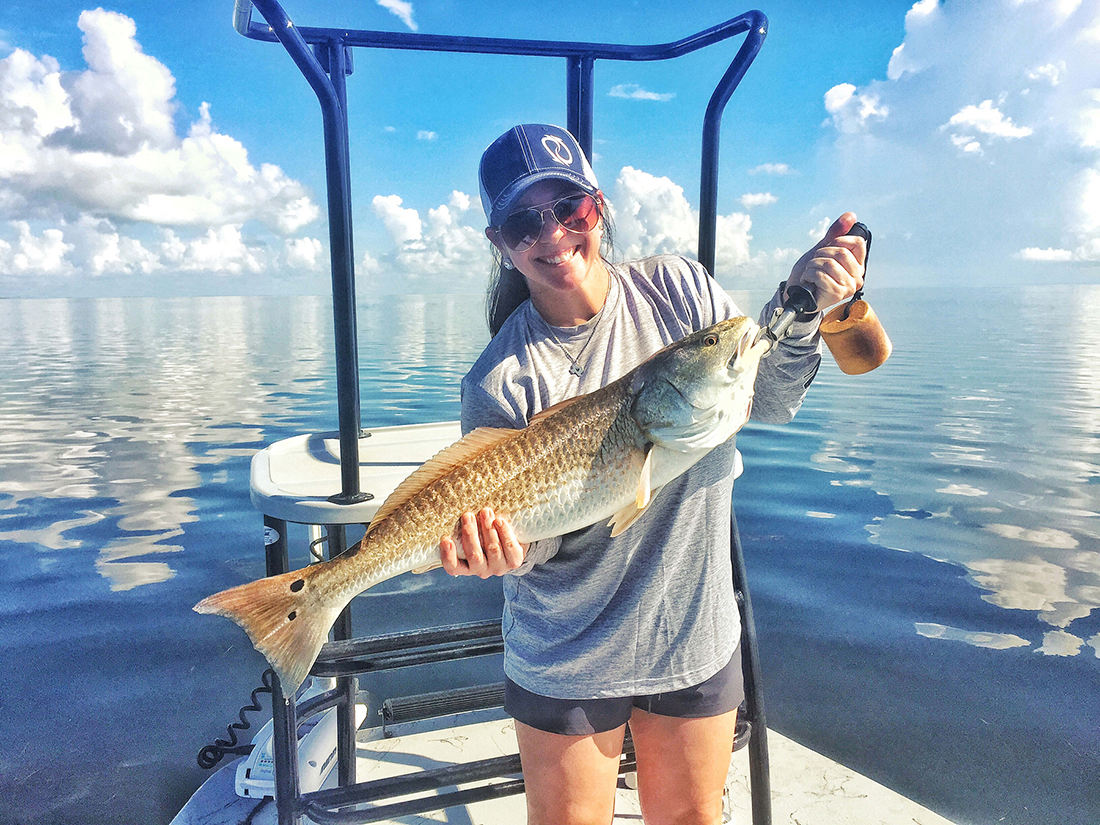 A woman on a boat holds a big fish that was just caught.