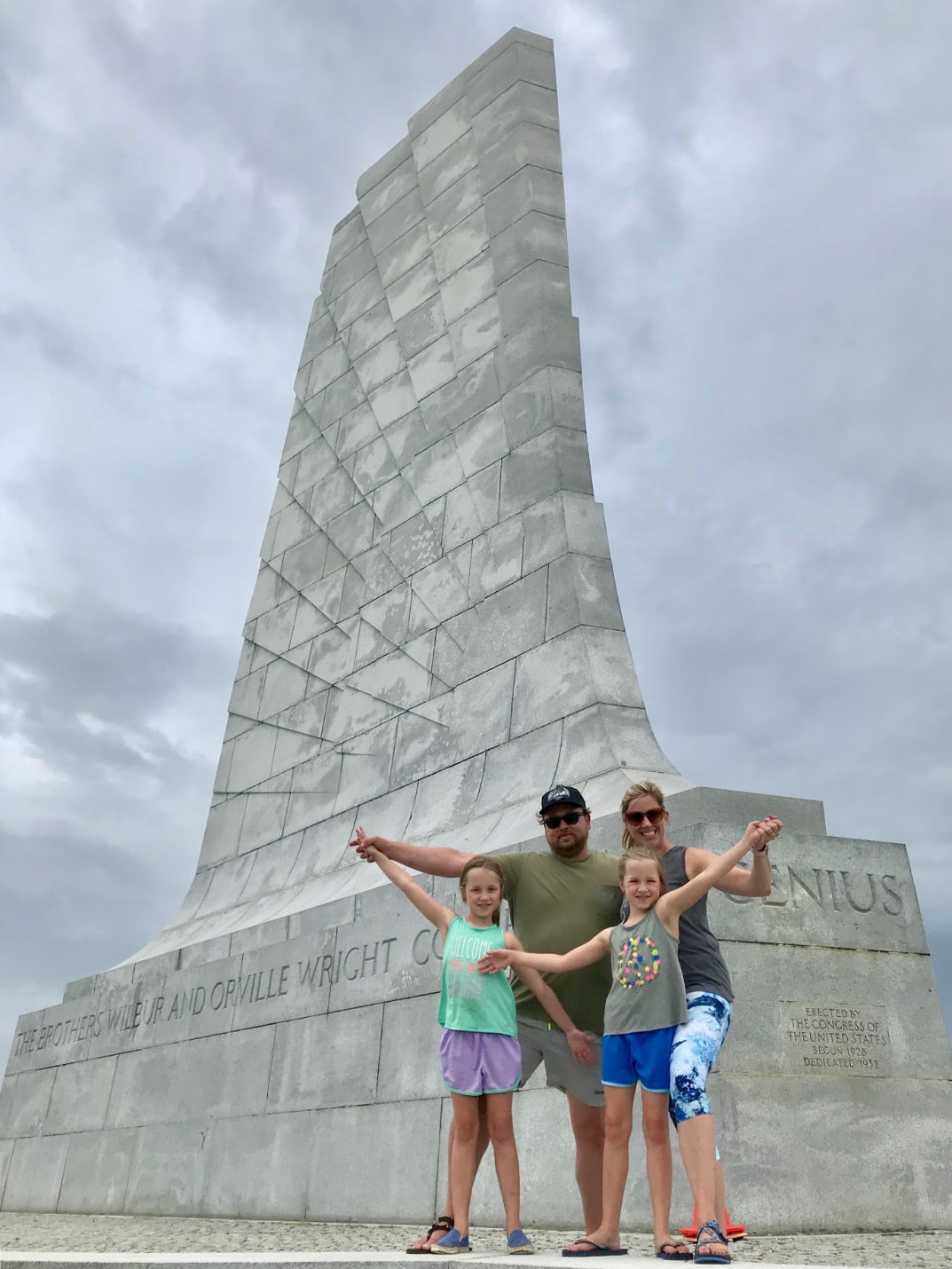 Young family of four posing in front of Wright Brothers Memorial