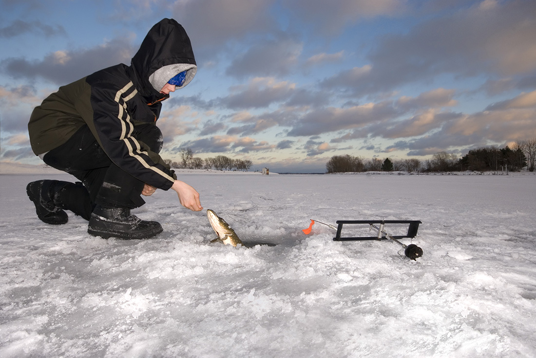 Young boy ice fishing on frozen surface.