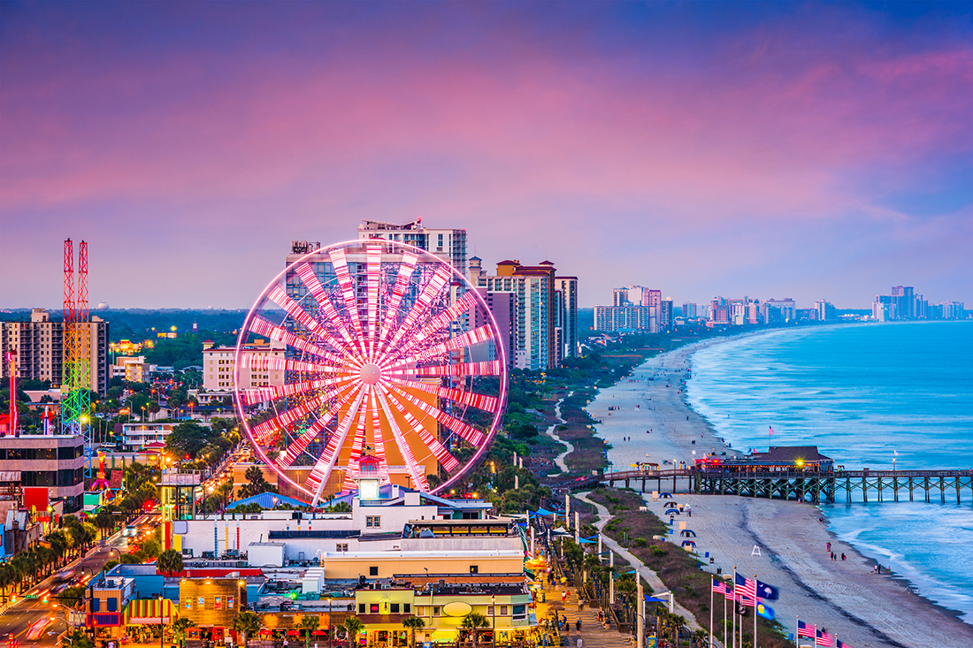 A neon-lit Ferris wheel close to a seashore.