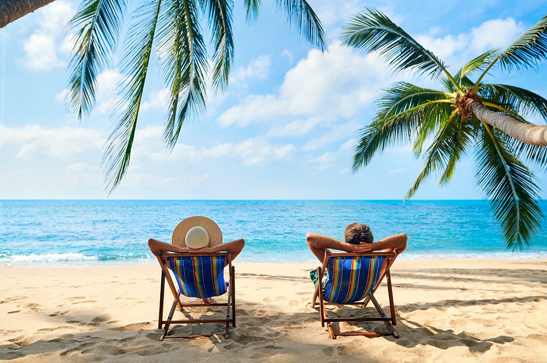 A man and woman lounge in the sand on a tropical beach.