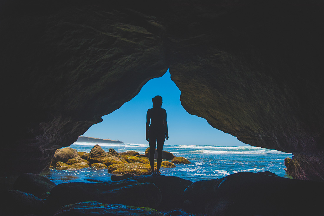 Woman standing in a cave looking out on the ocean in Sunset Cliffs.