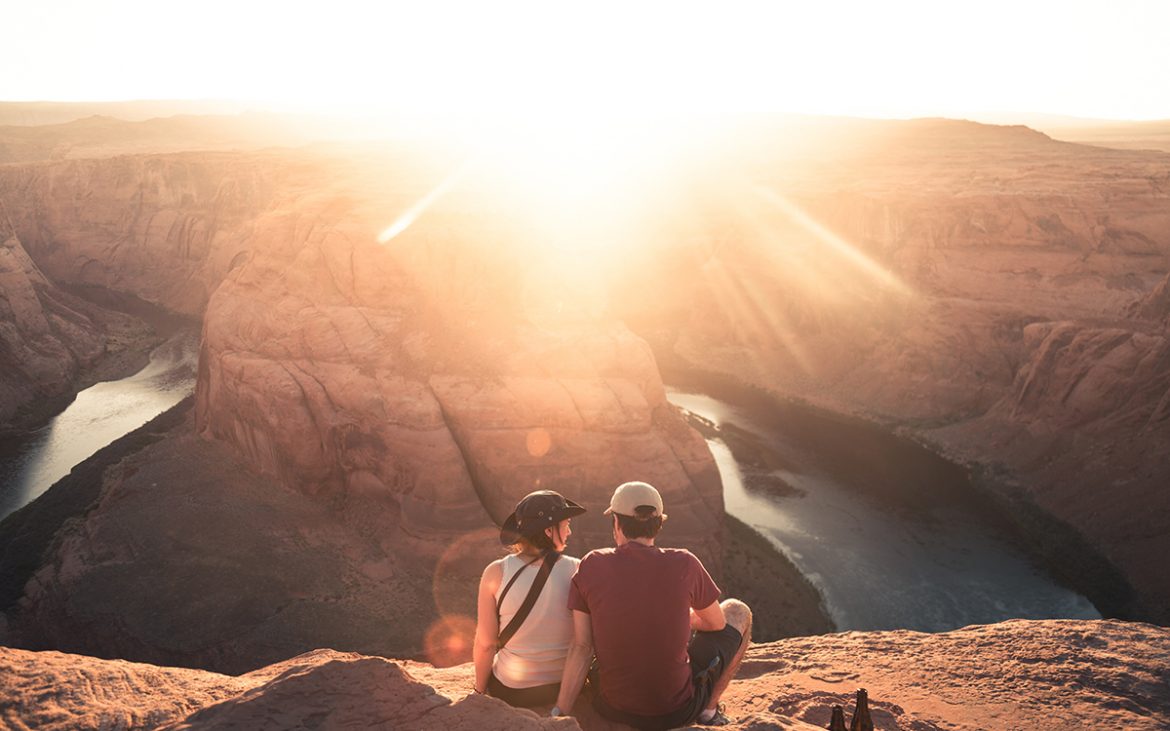 A couple sitting on a cliff overlooking a sunset.