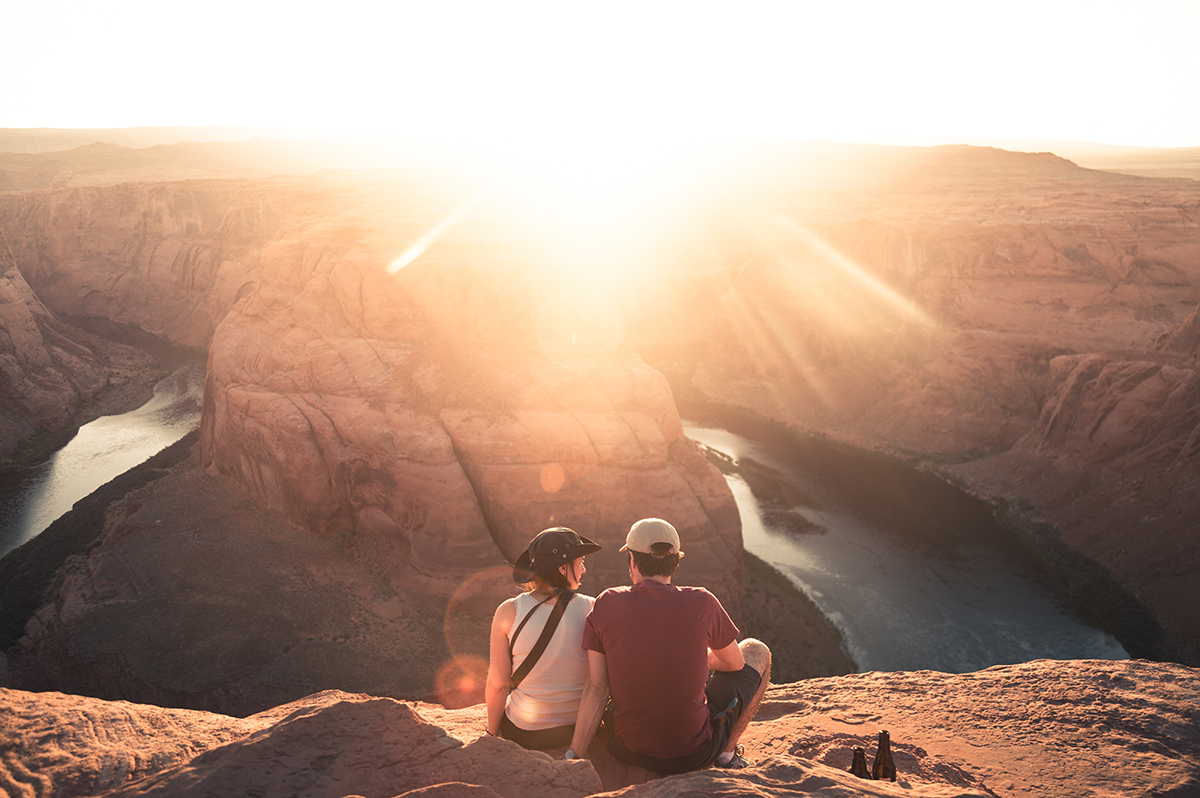 A couple sitting on a cliff overlooking a sunset.