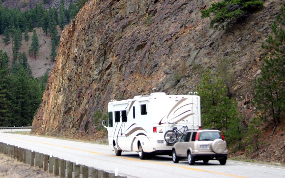 An RV driving along a road carved into a mountainside.