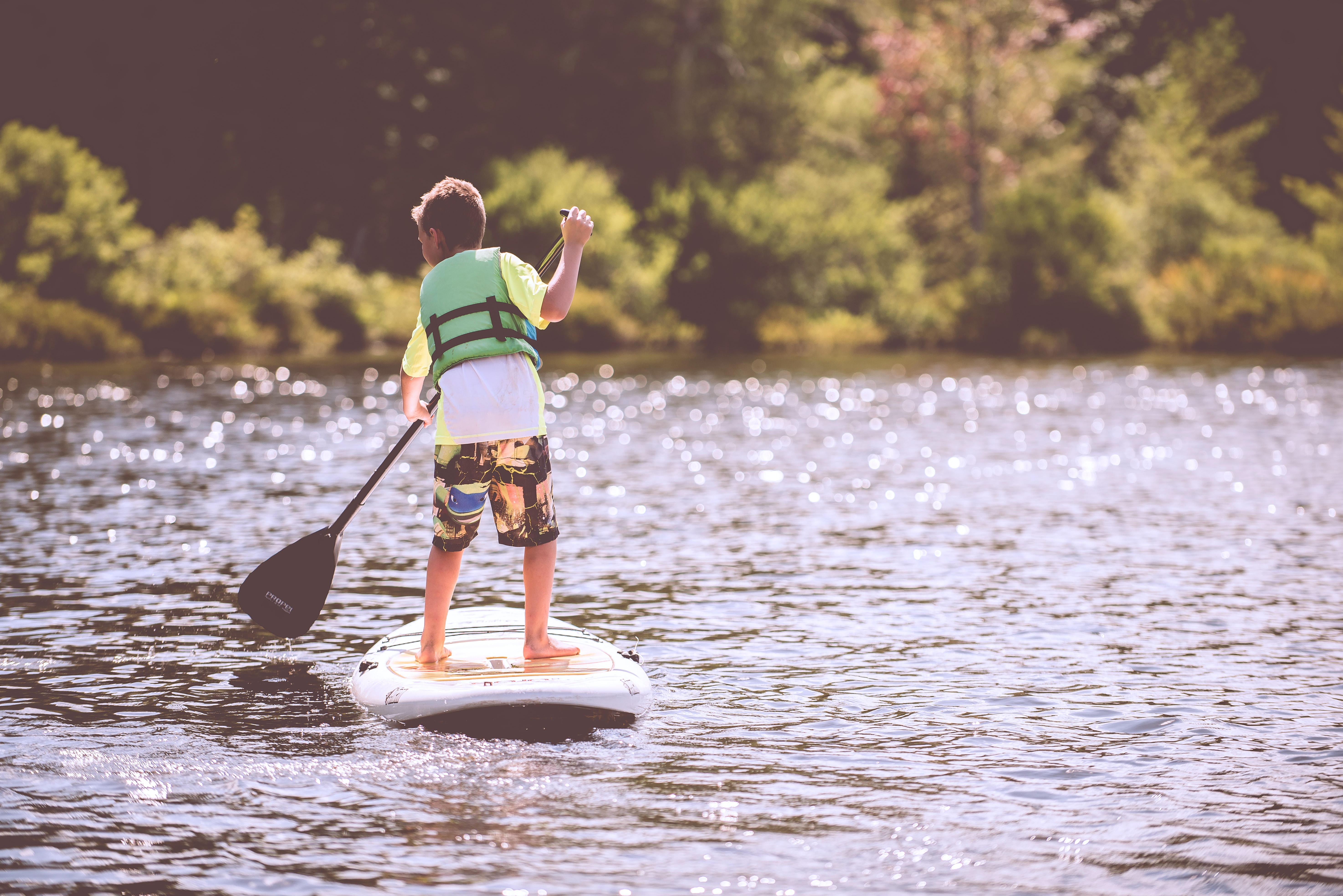 A kid goes paddleboarding on a lake.