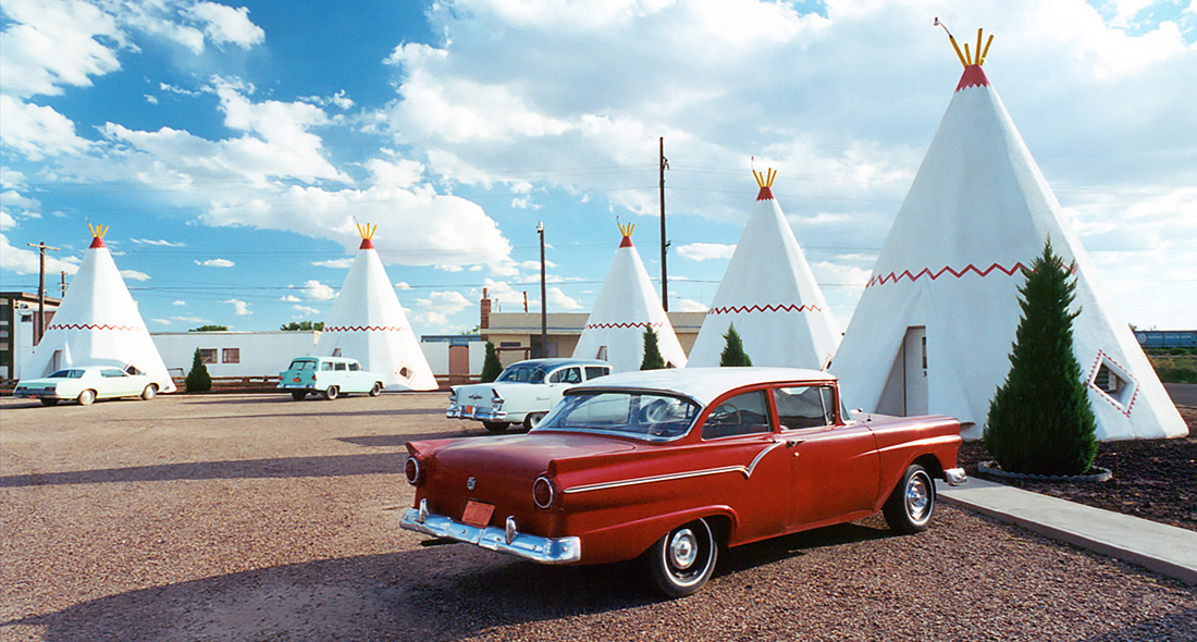 Classic cars parked next to white tents.