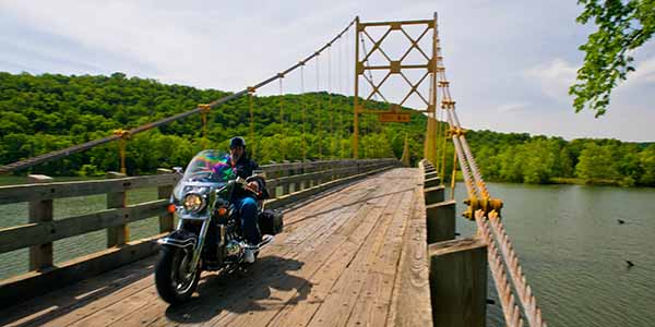 A motorcyclist riding over a suspension bridge.