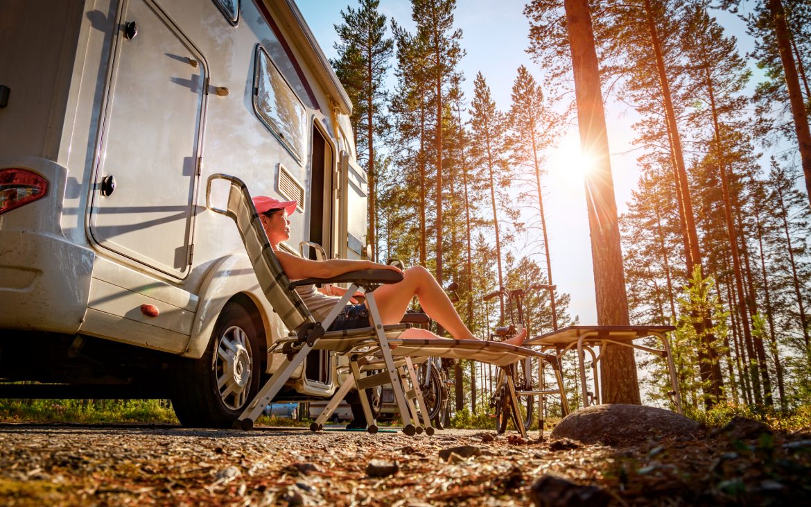 Woman lounging on outdoor chair next to RV in woods
