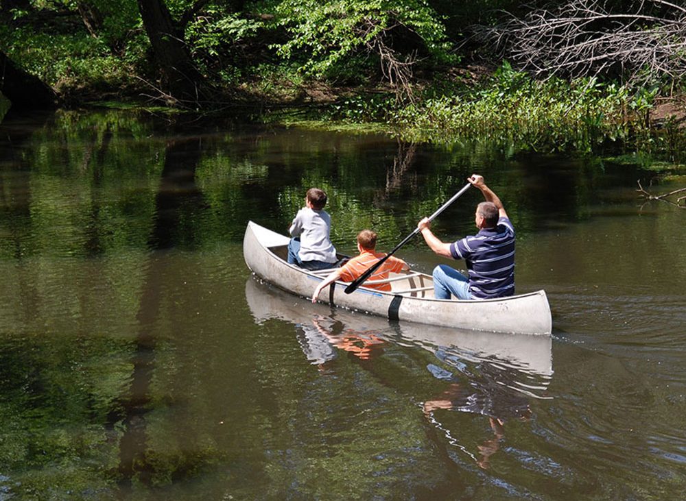 A man paddling a canoe with kids.