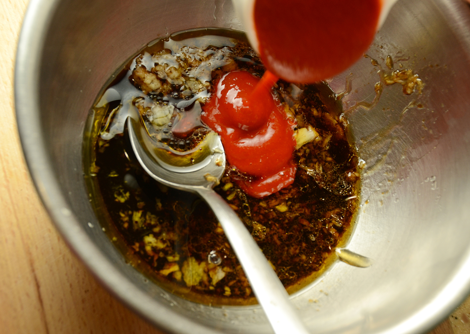 Stainless steel bowl with spoon and mixing sauce.