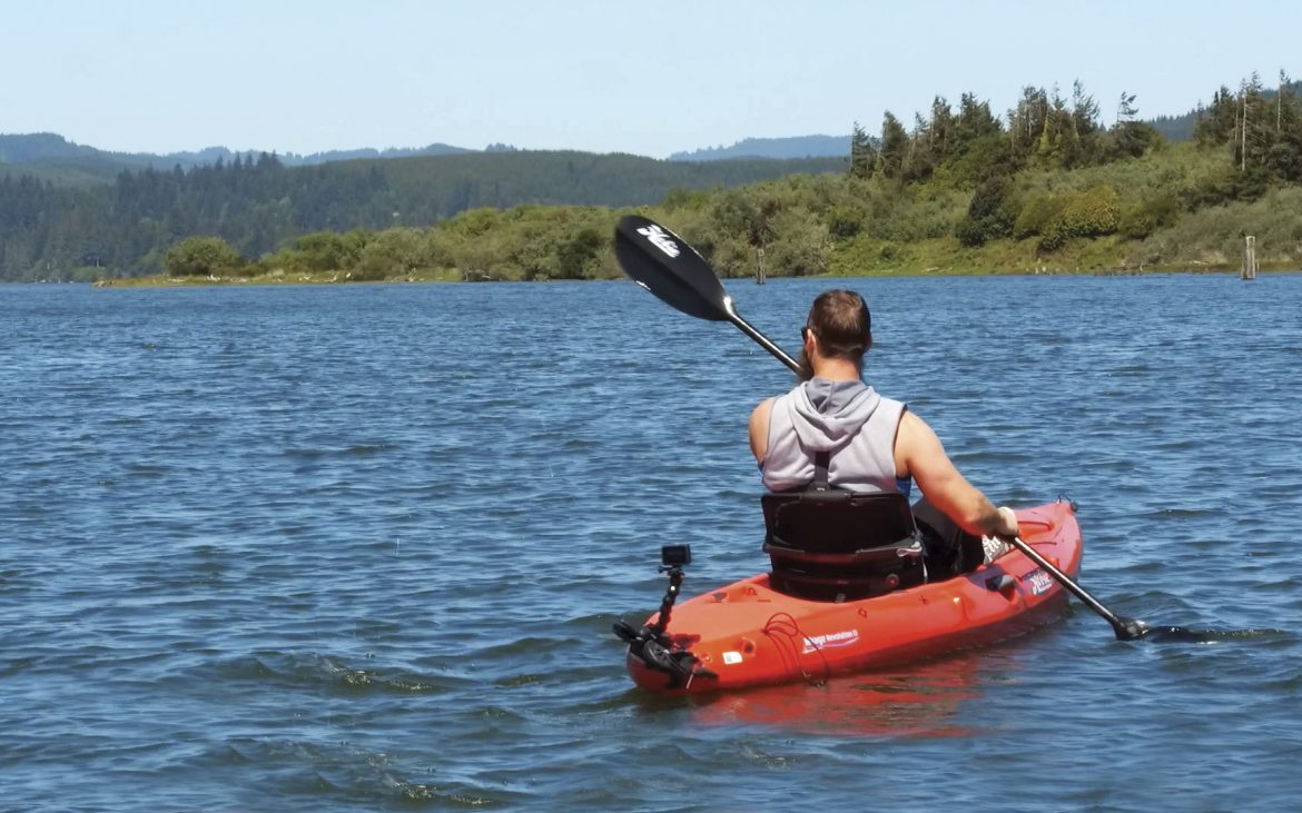 Man kayaks on a lake with wooded banks.