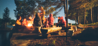 Young adults and kids around a campfire next to lake
