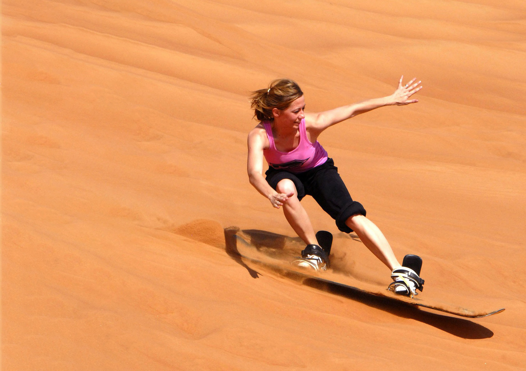 A woman rides down a dune on a sandboard.