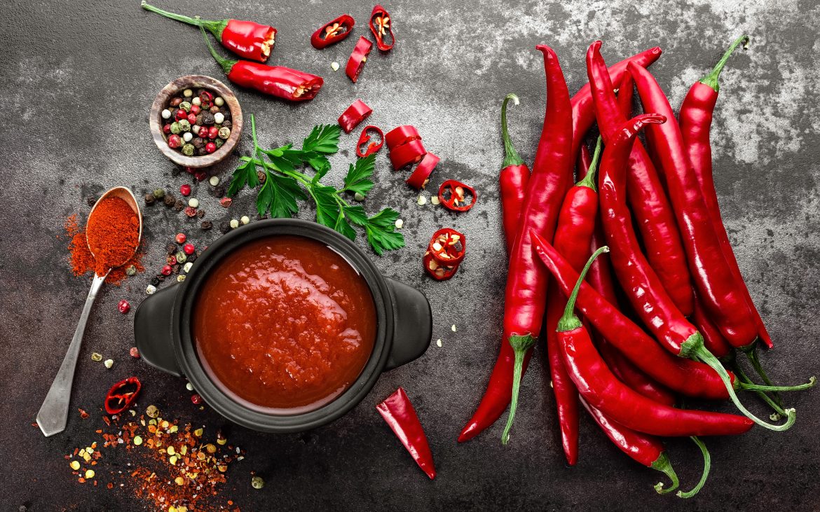 Spicy chili sauce, ketchup, red chilis on dark background
