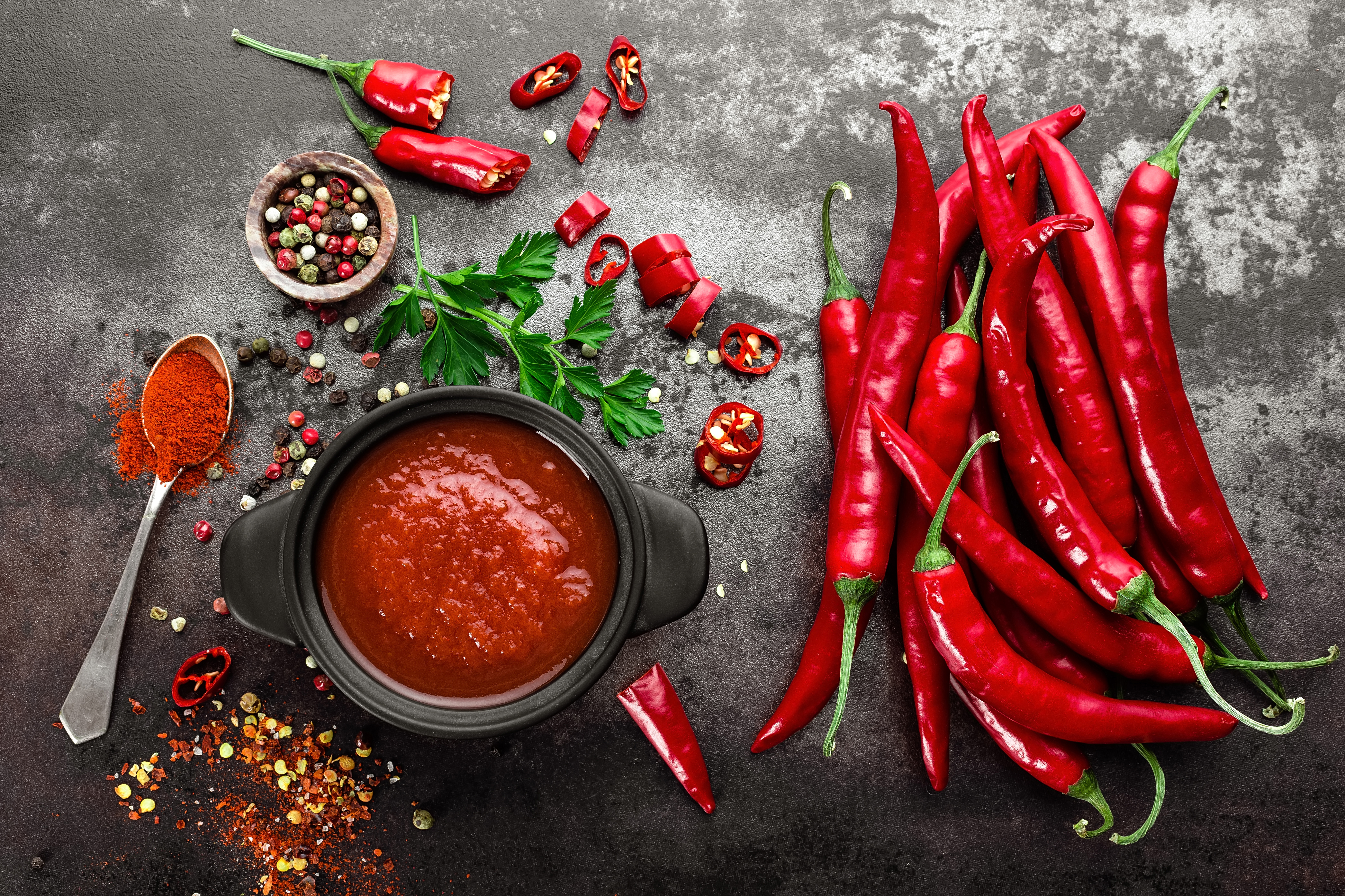 Spicy chili sauce, ketchup, red chilis on dark background