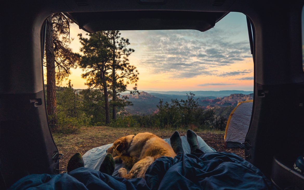 Two people lying in back of van with dog and view of sunrise over cliff in Sedona Arizona