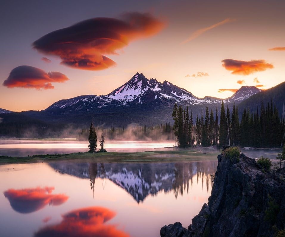 A mountain is reflected on a placid lake during sunset.