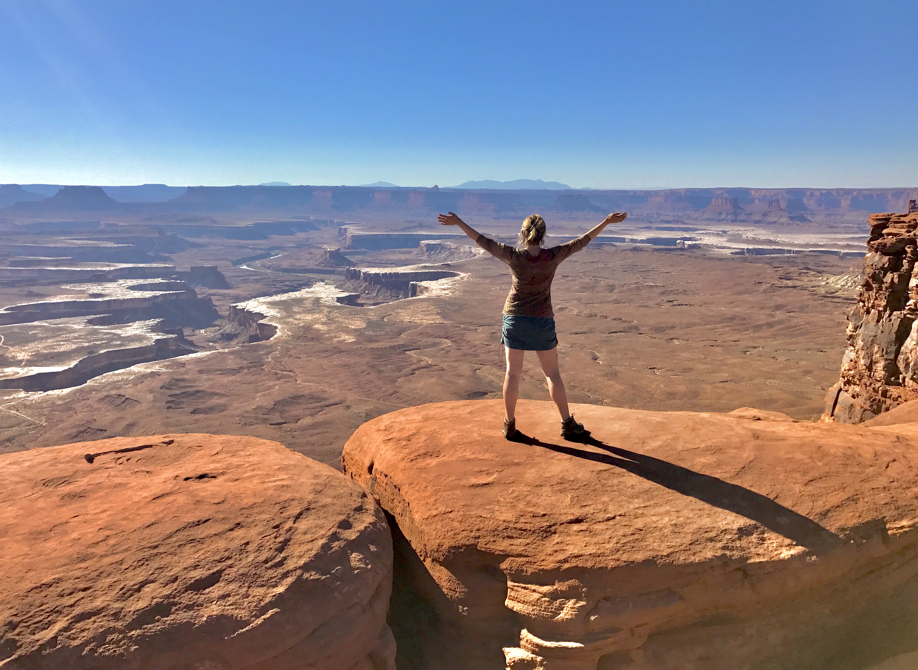 A woman with arms outstretched looking out at a canyon.