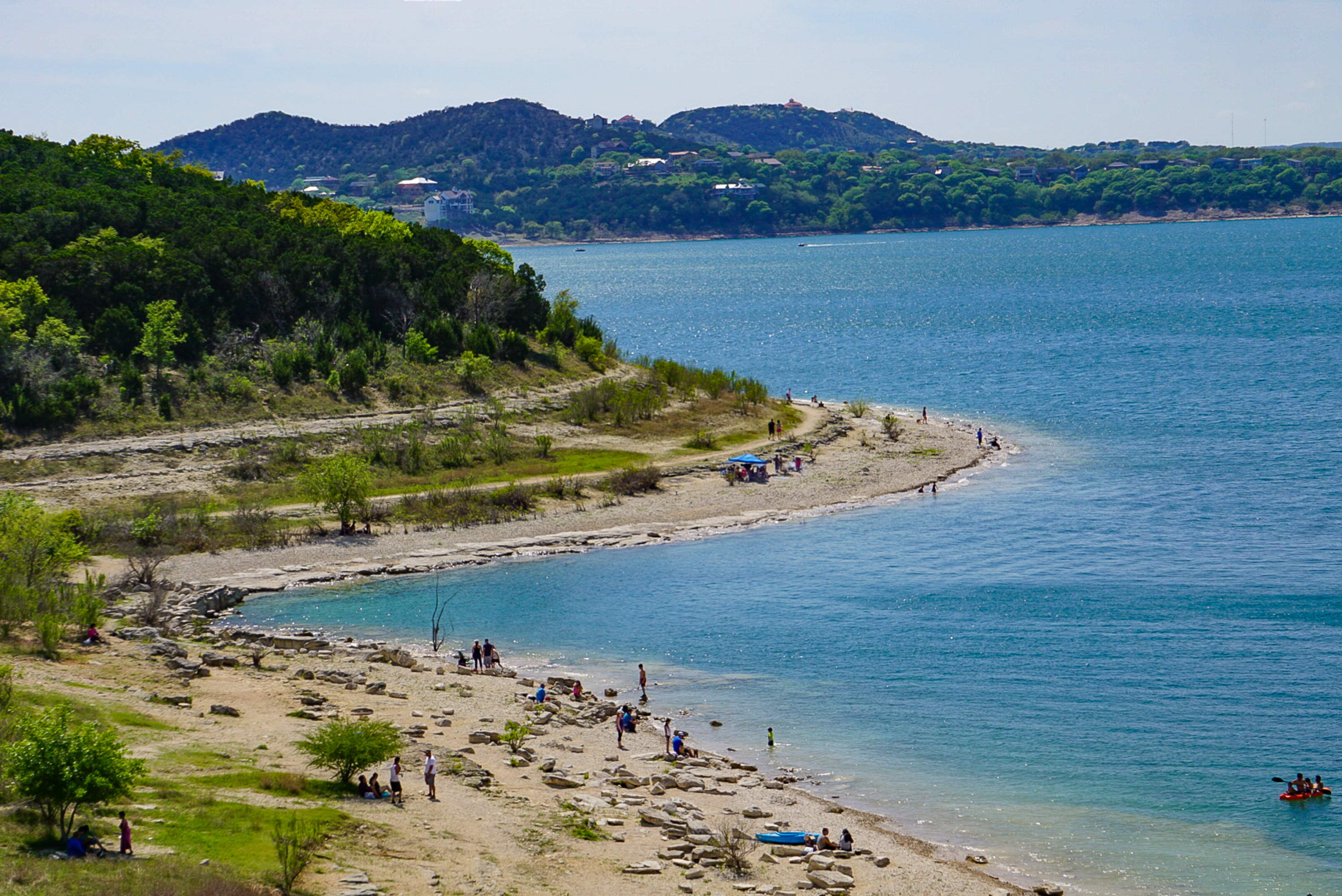Shoreline of a lake with beachgoers on the sand.