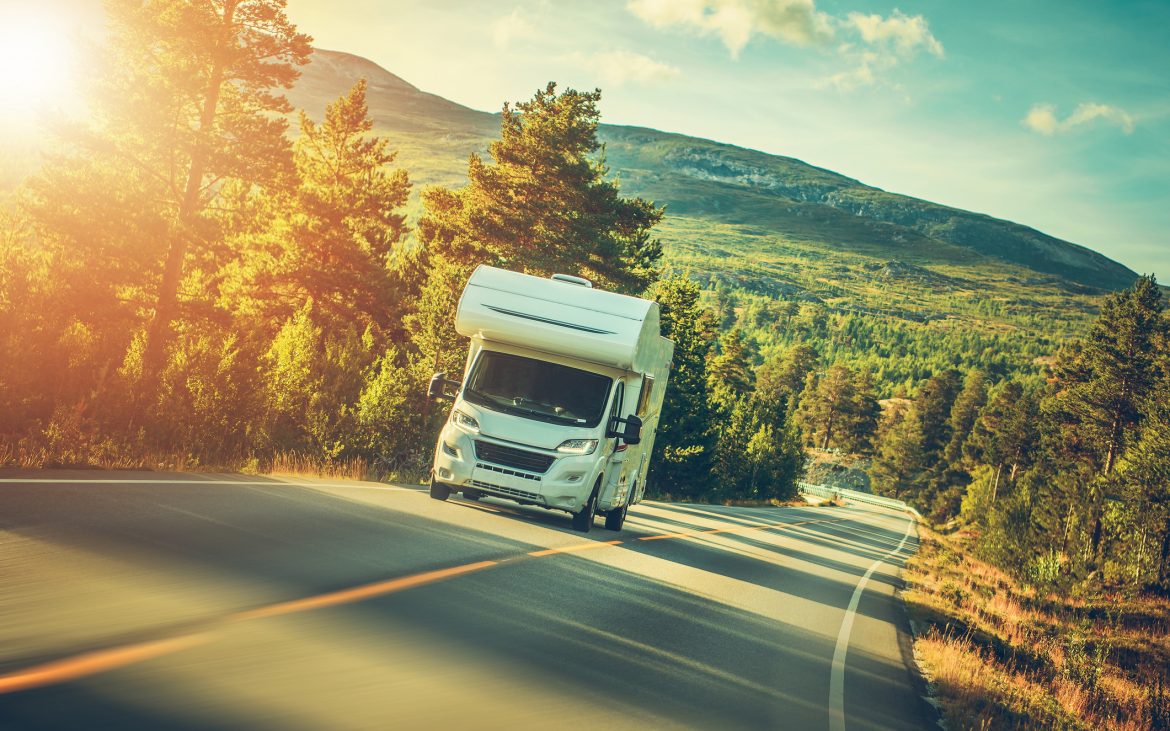 The road ahead for 2021 -- An RV driving on a forested highway with sunlight streaming through.