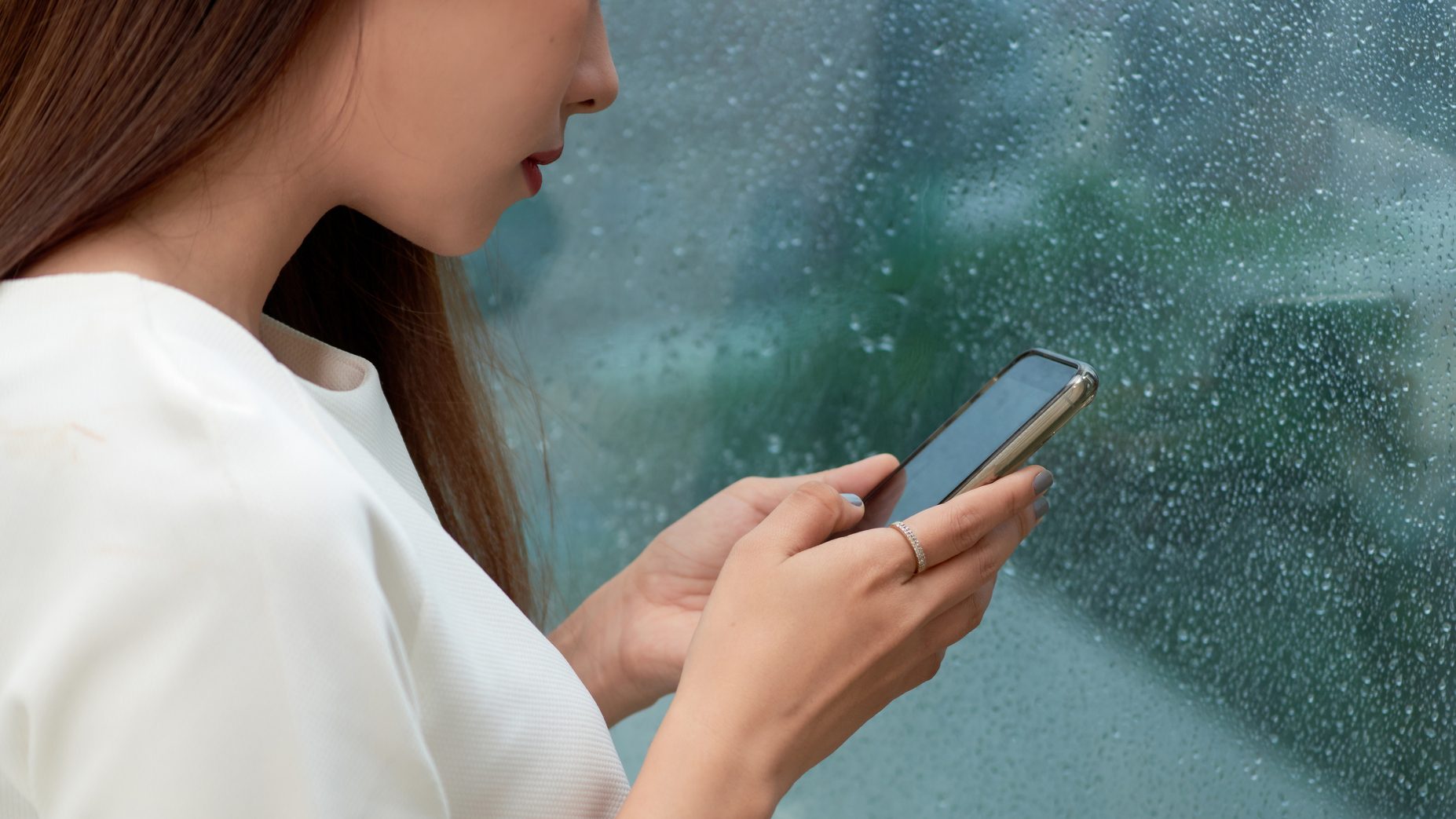 Side view portrait of a serious woman using a smart phone in a rainy day at home