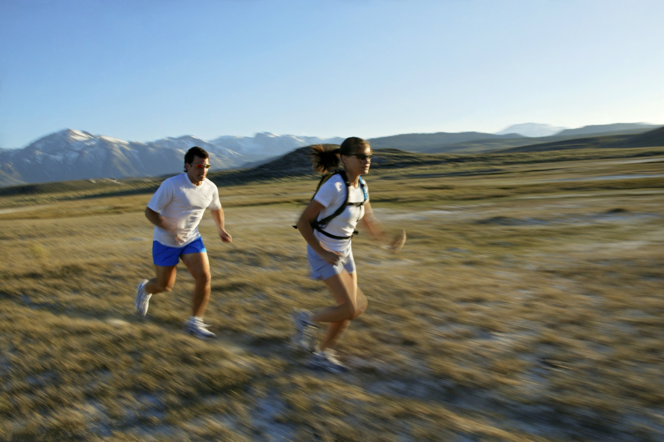 A couple run along a trail with mountains in the background