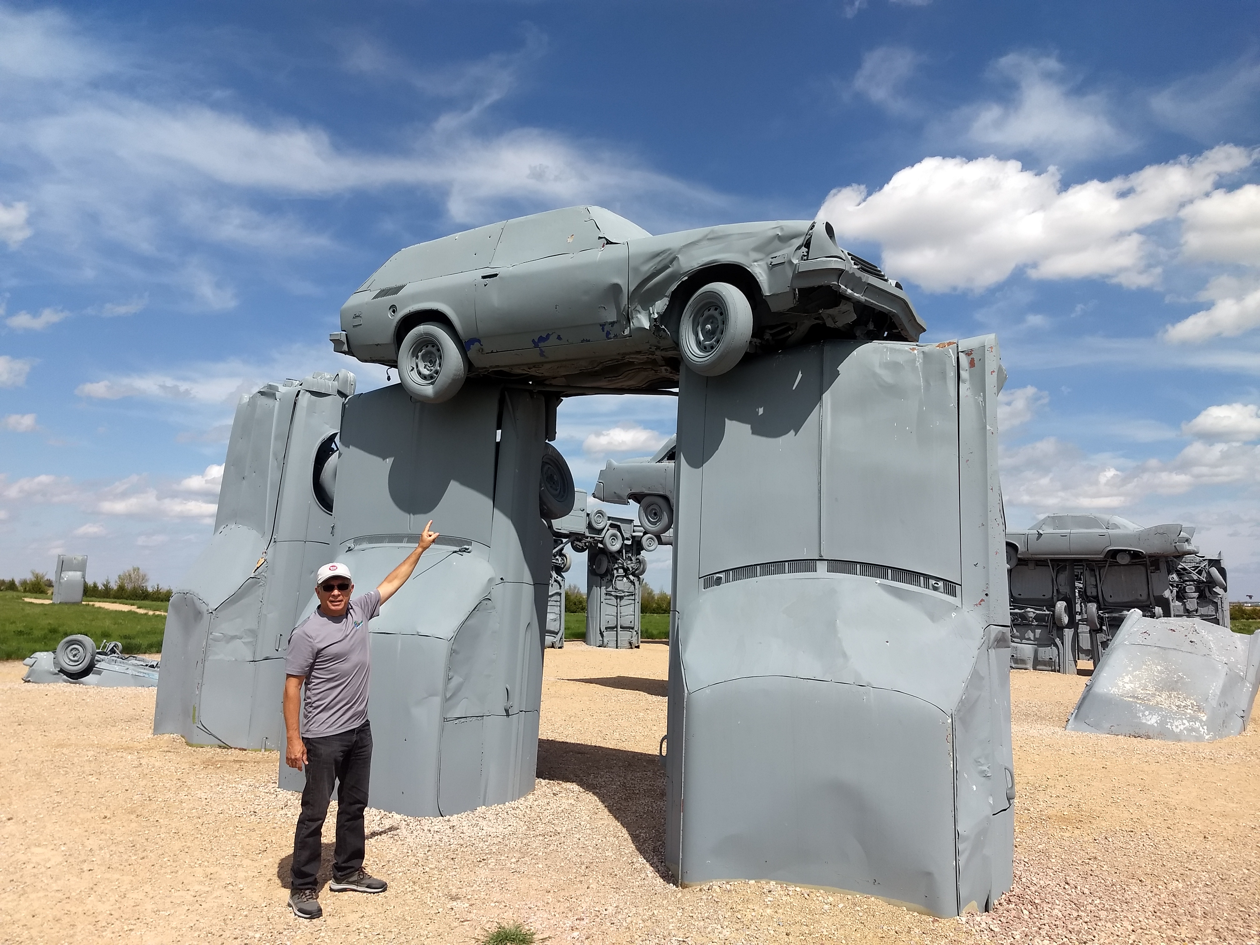Call of the Highway — Man standing in front of cars stacked in Stonehenge Configuration.