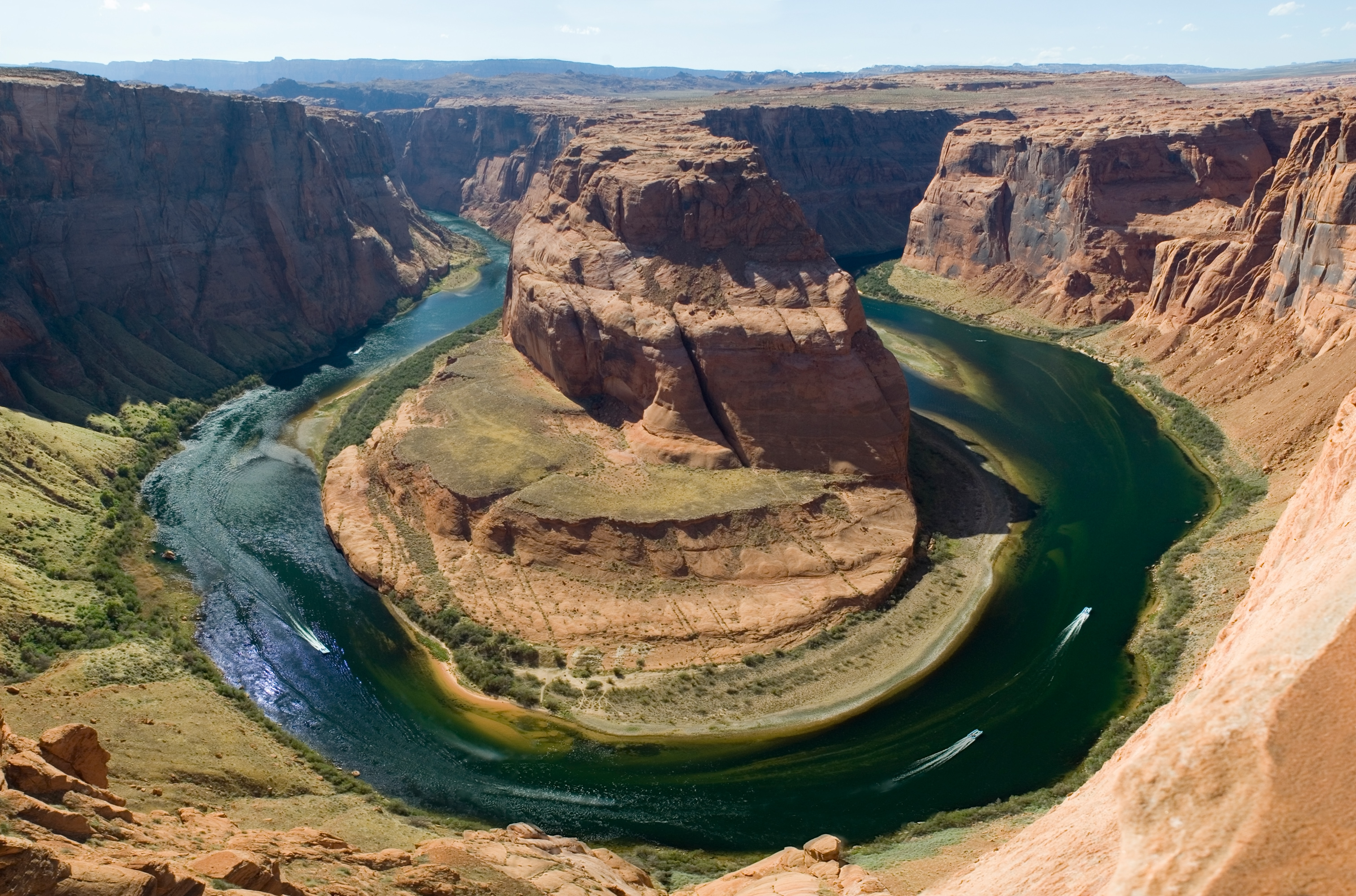 Boats follow the extreme curve of a river at the bottom of a canyon..