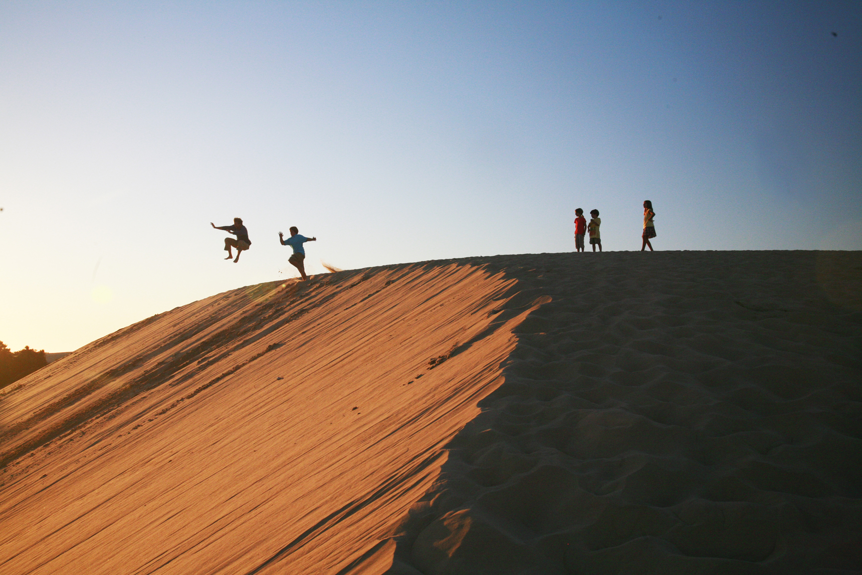 Wander North Carolina's Outer Banks —People jumping off a huge sand dune.