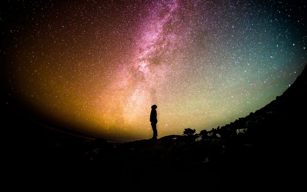A lone figure looks up an a starry sky.