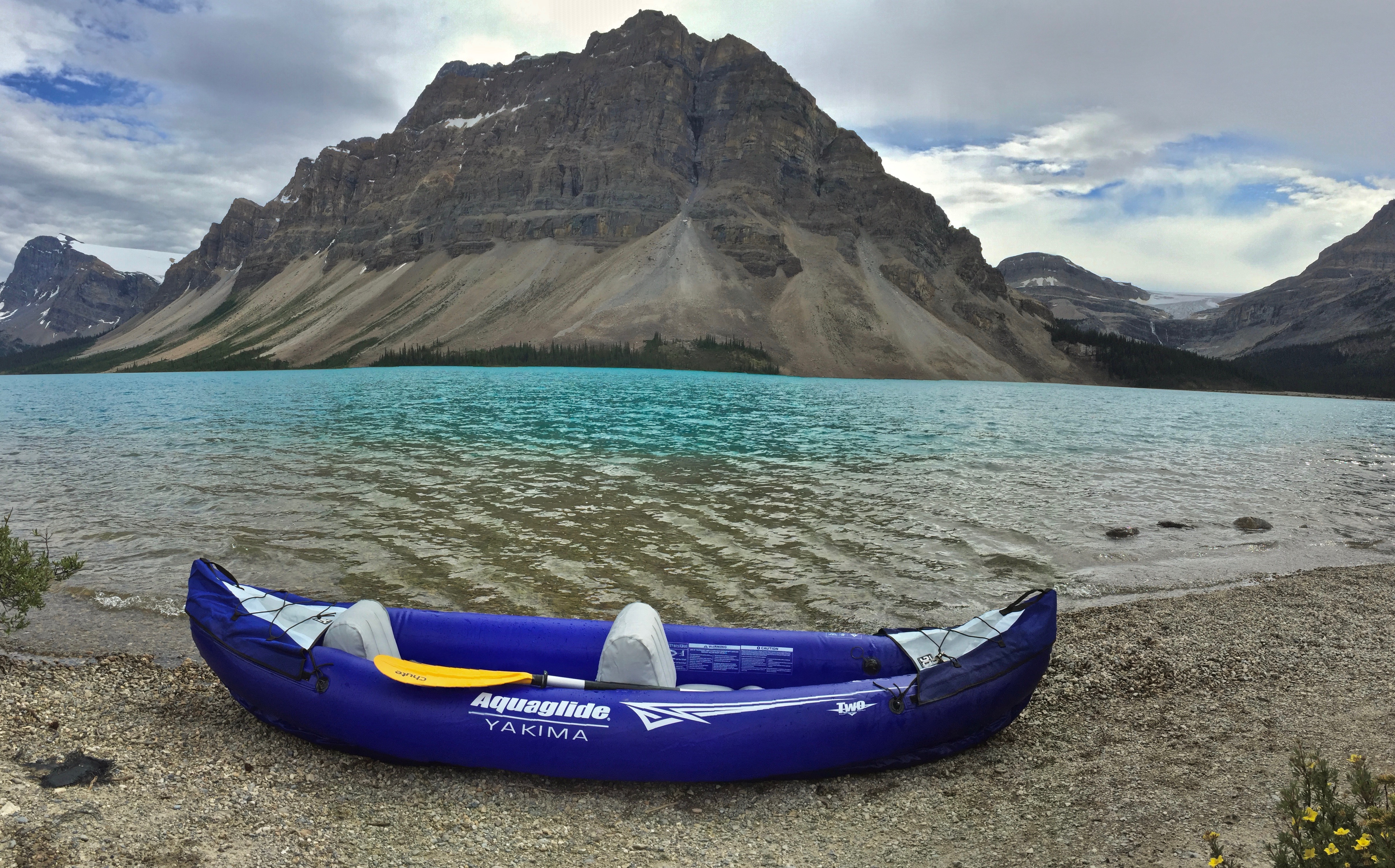 A blue inflatable kayak lies on the banks of a sprawling river.