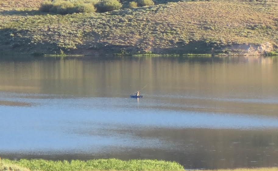 Occupant of a lone boat in a vast lake casts a line.