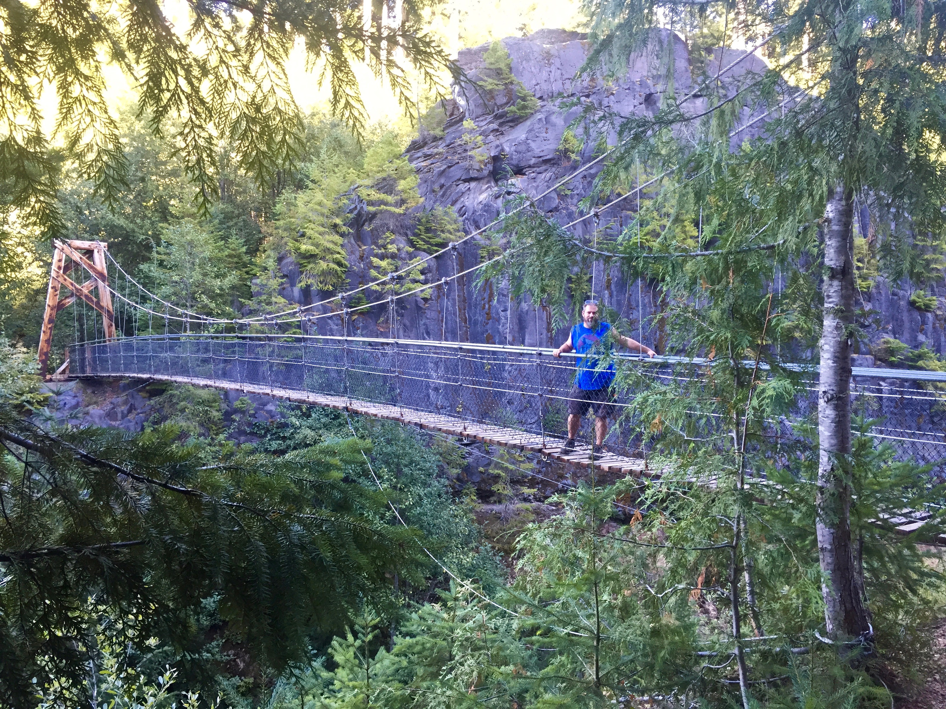 Man crossing rope bridge across a ravine.
