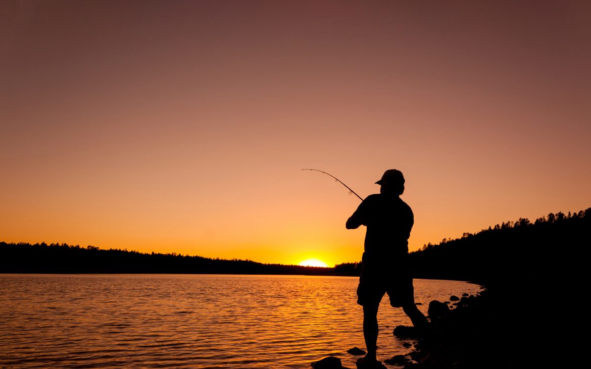 Man casts a line as the sun rises on the horizon.