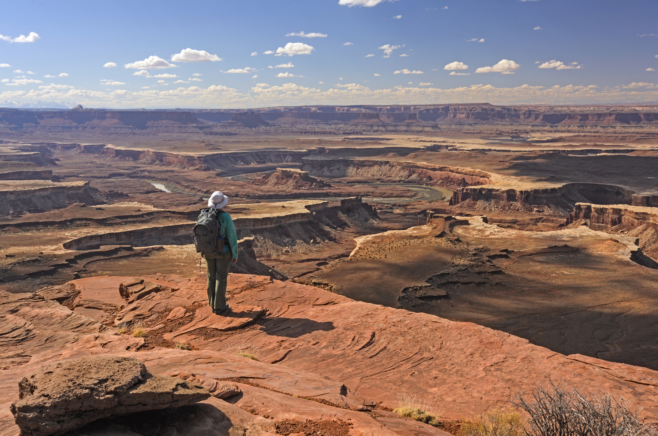 A lone hikers stands on the edge of a cliff and looks out at a landscape of cliff faces and ridges.