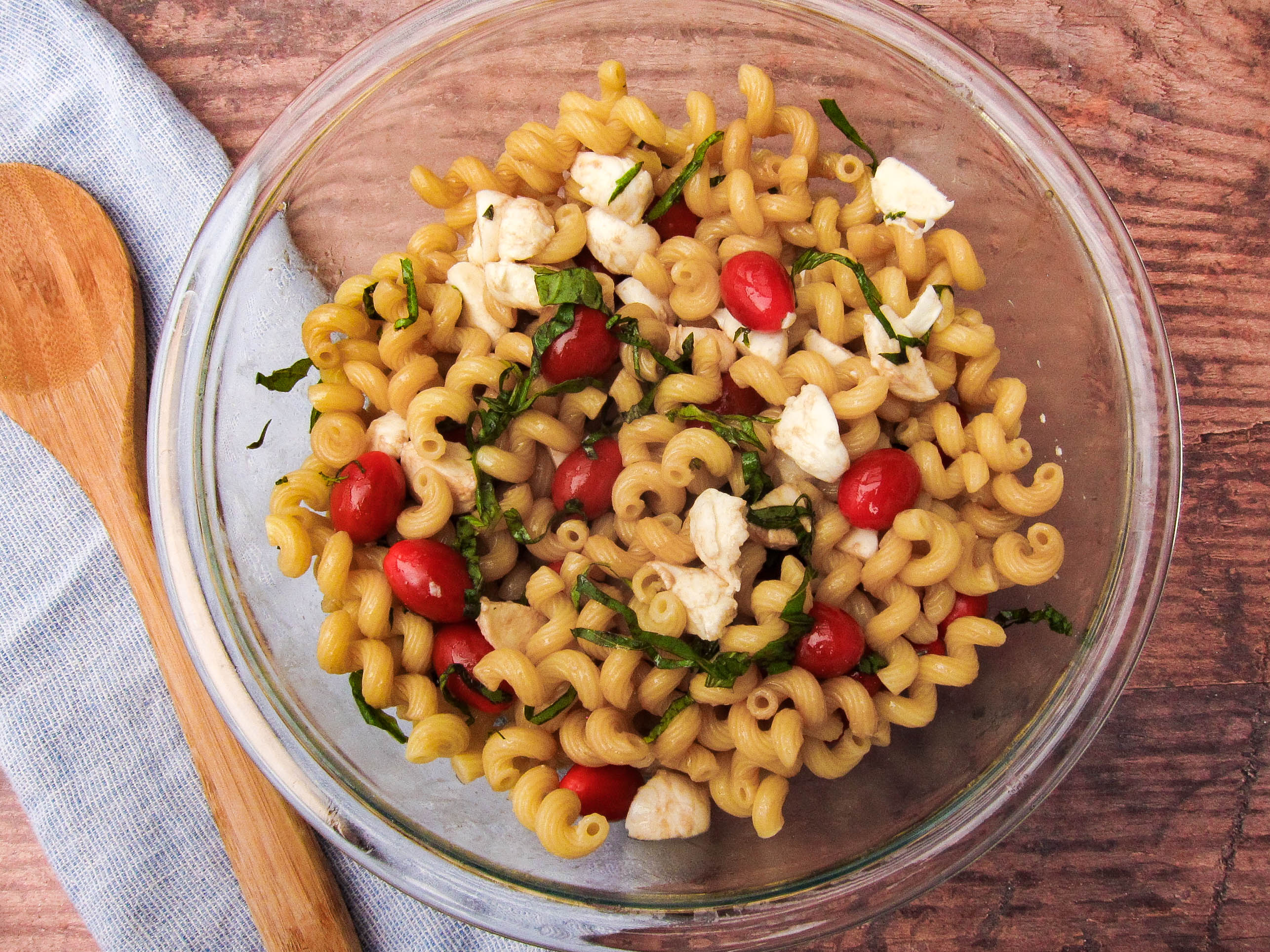 Bowl of pasta salad with wooden spoon.