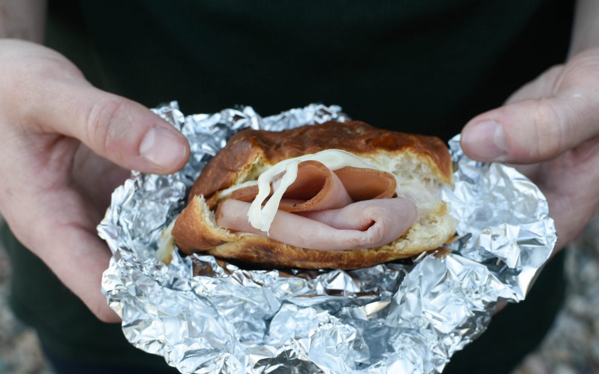 Foil-wrapped Campfire Sandwiches Hands holding a ham and cheese sandwich in foil.