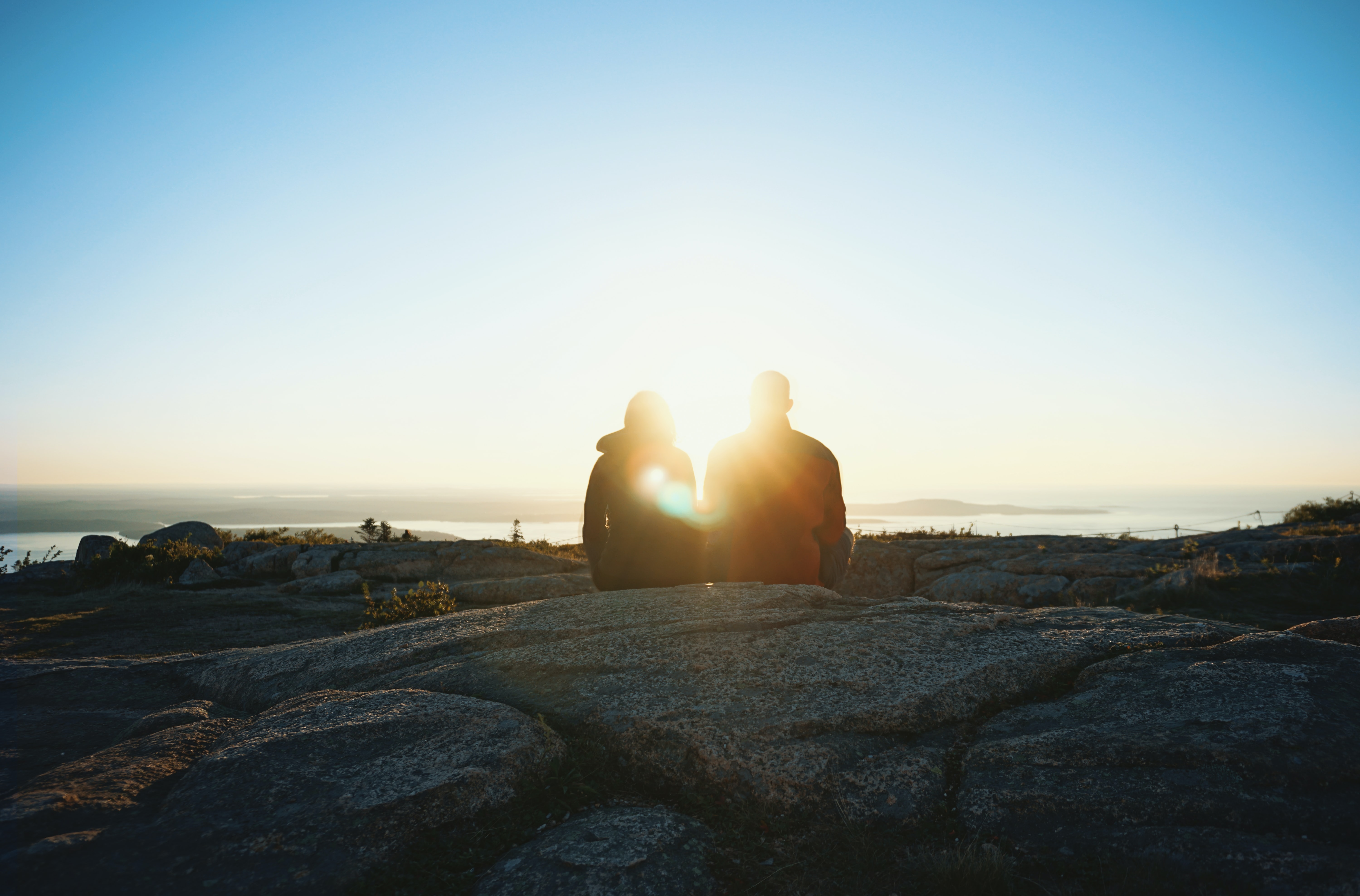 A couple watch the sunrise from atop a mountain.