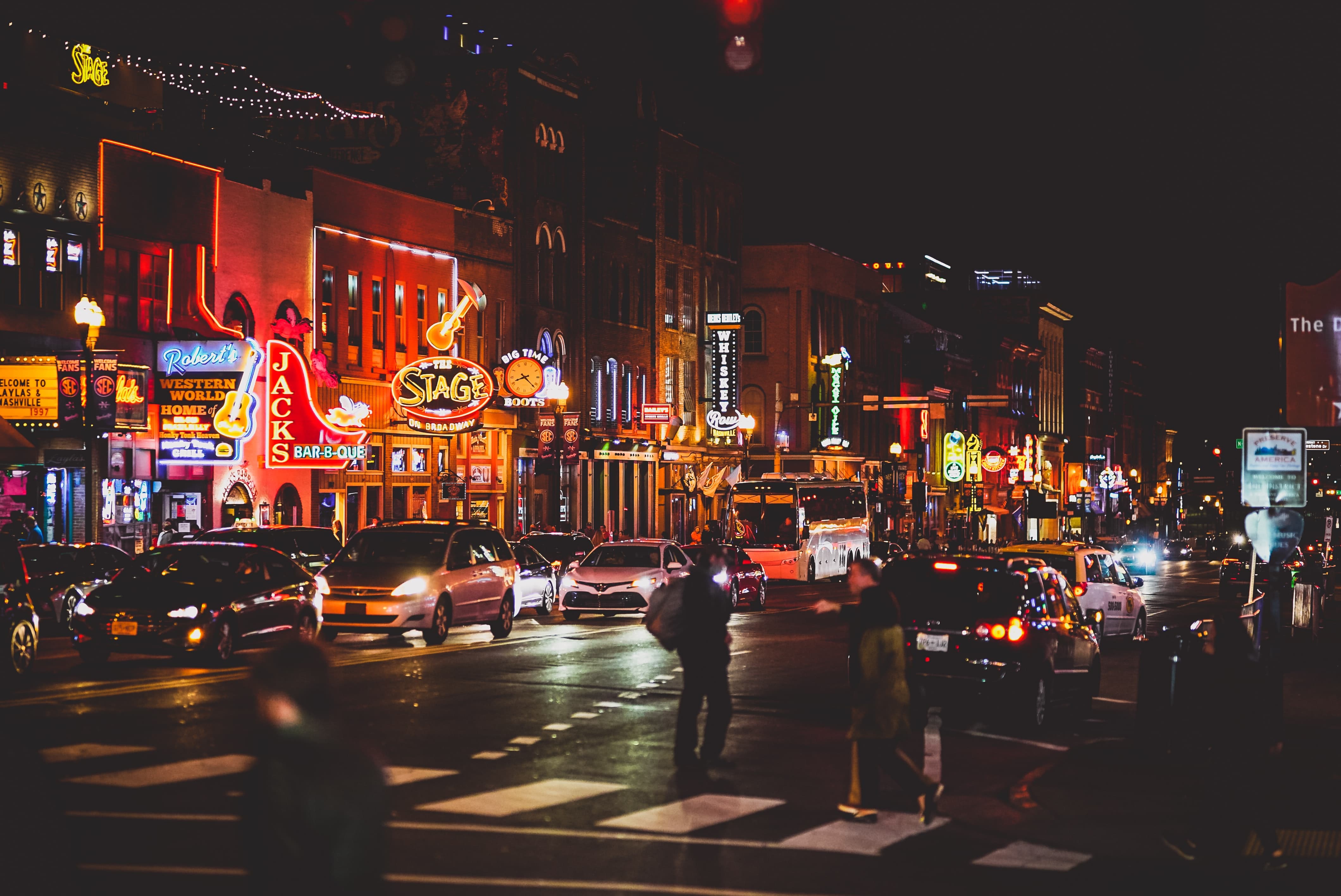 Pedestrians walk along a street lined with nightclubs and neon lights.