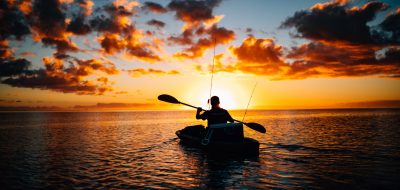 A man kayaks toward a beautiful red sunset.