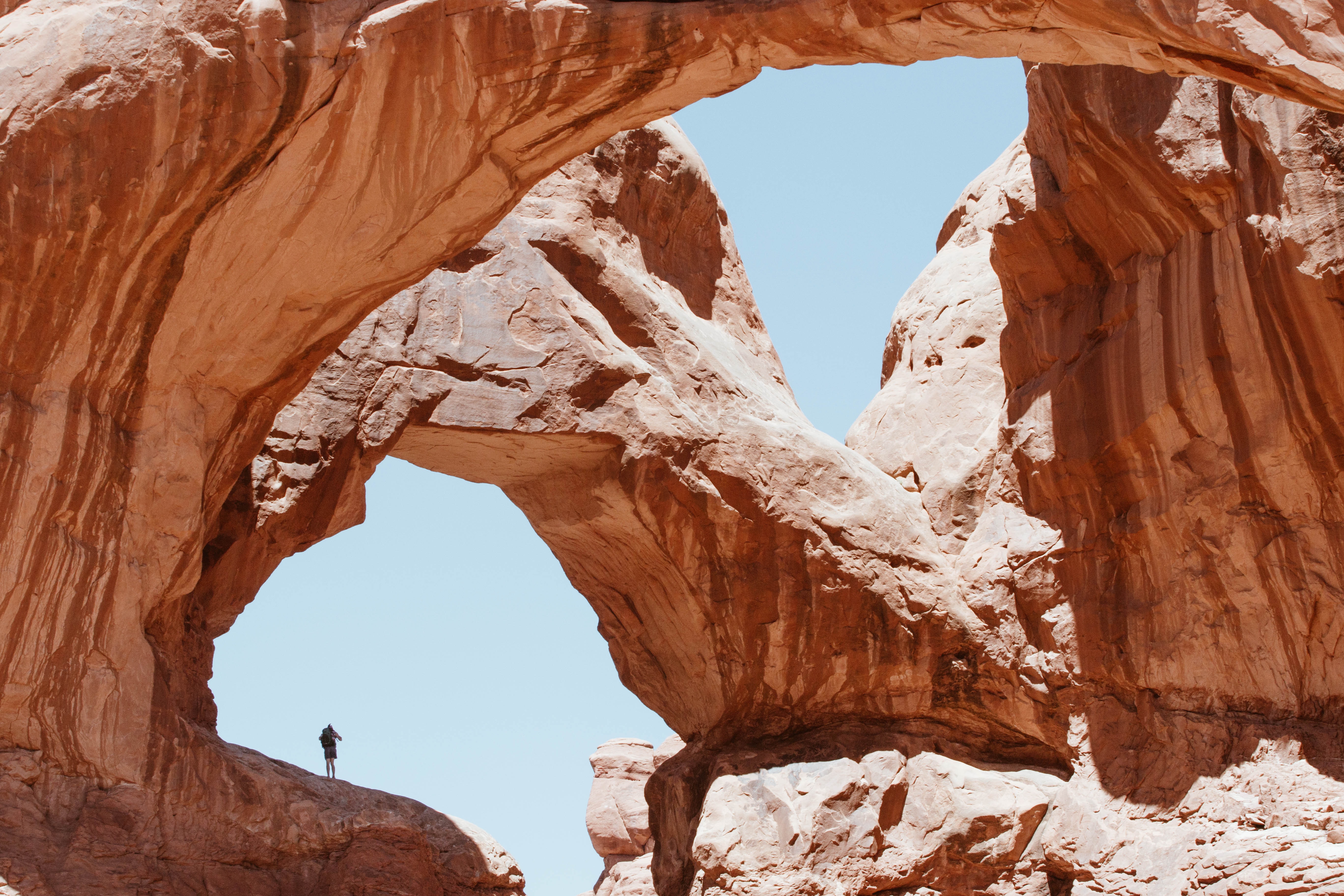 A lone hiker appears tiny against towering rock arches.