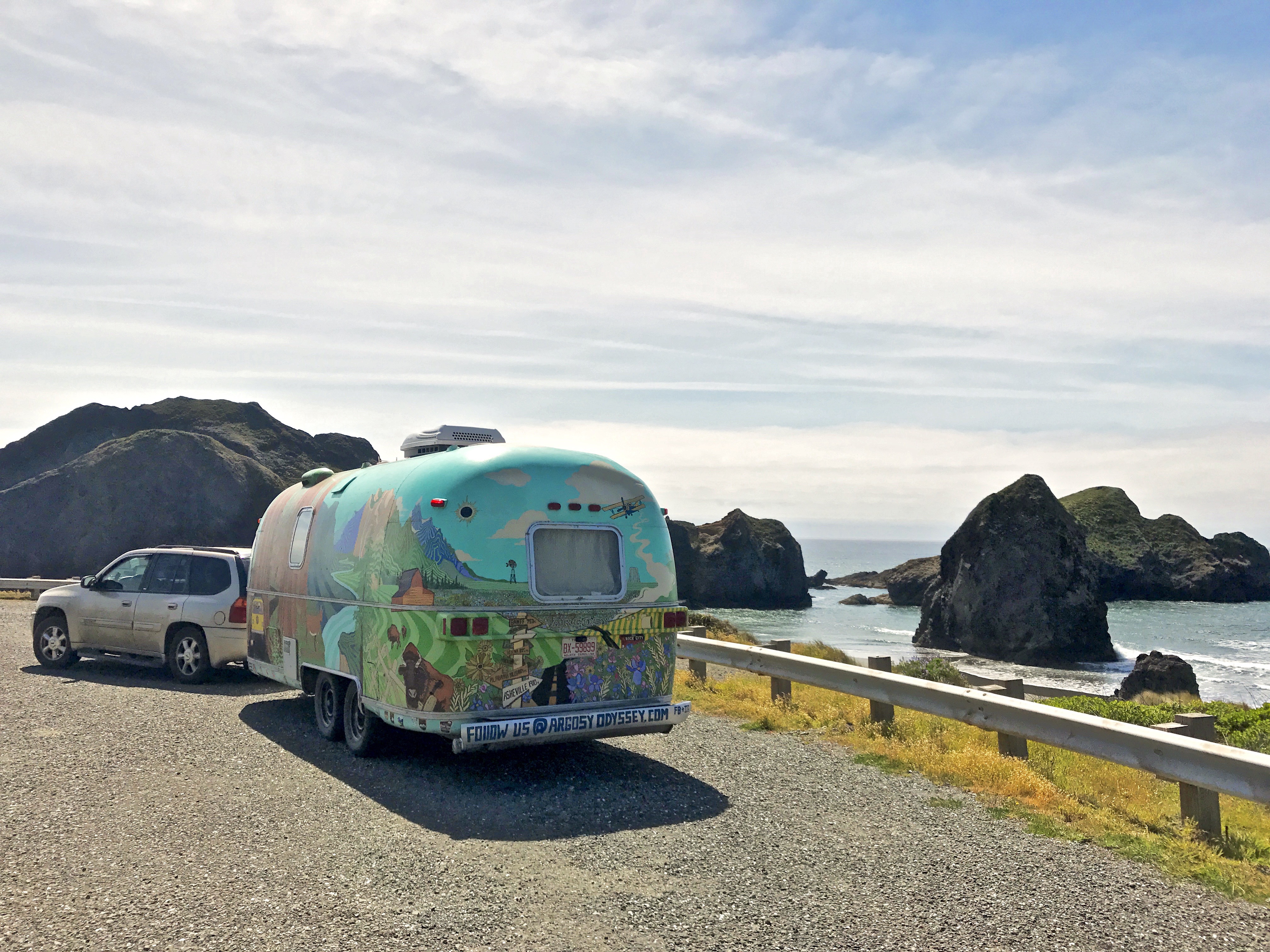 A colorful Airstream trailer parked on a coastline with sea stacks in background.