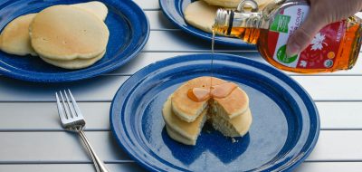 Blue plates with pancakes on them and syrup being poured on one plate