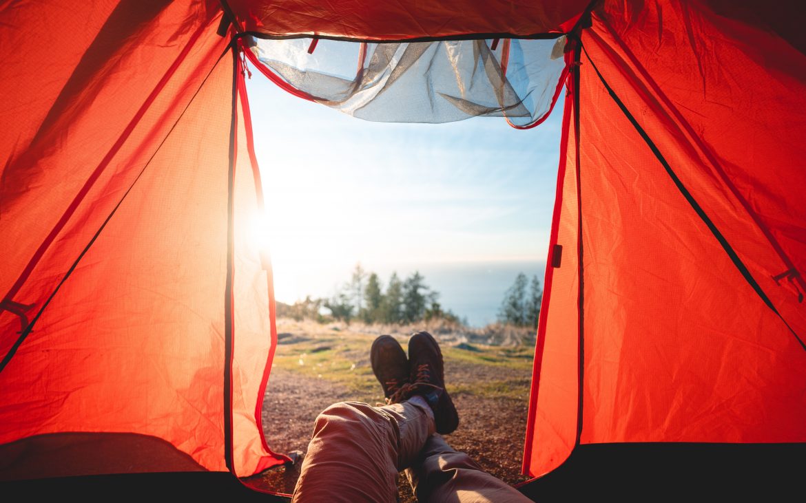 Man's legs hanging out of tent with lake view