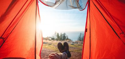 Man's legs hanging out of tent with lake view