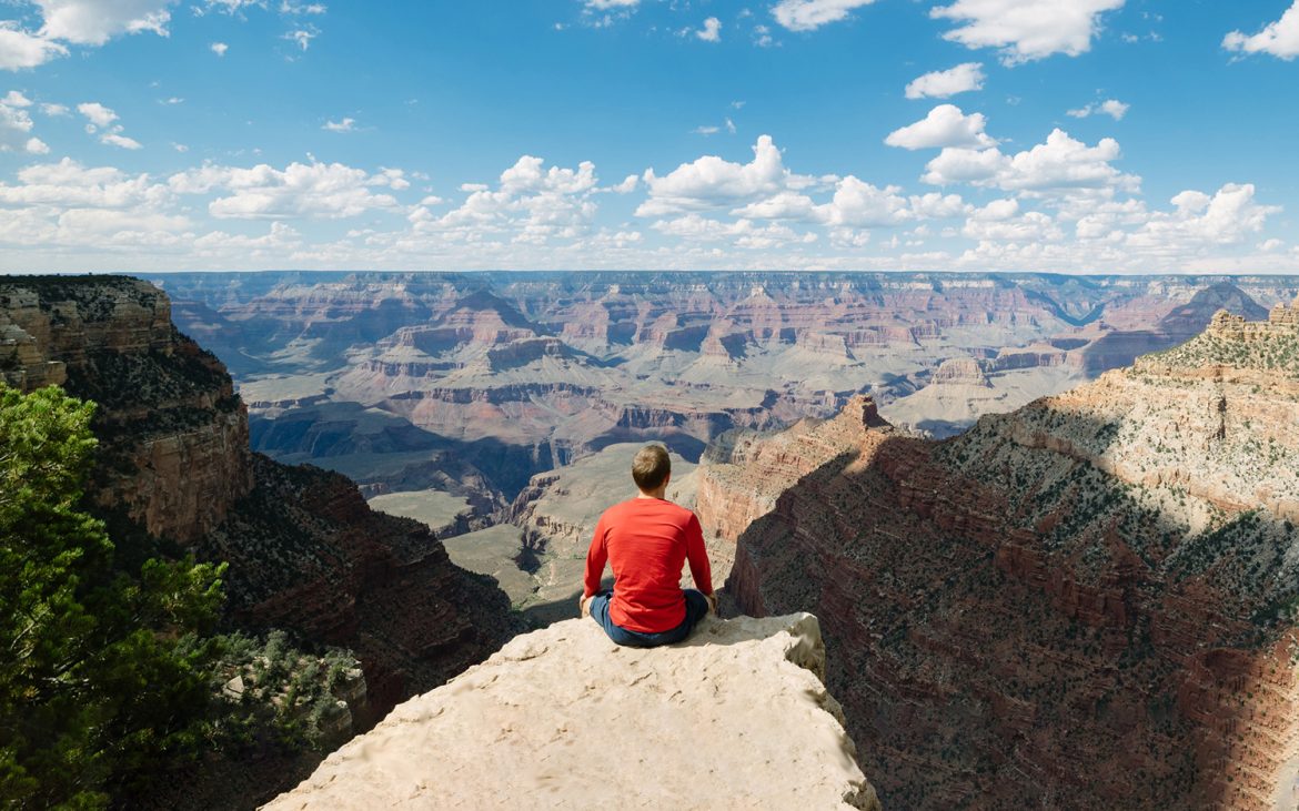 Man sits perched on the rim of epic canyon.