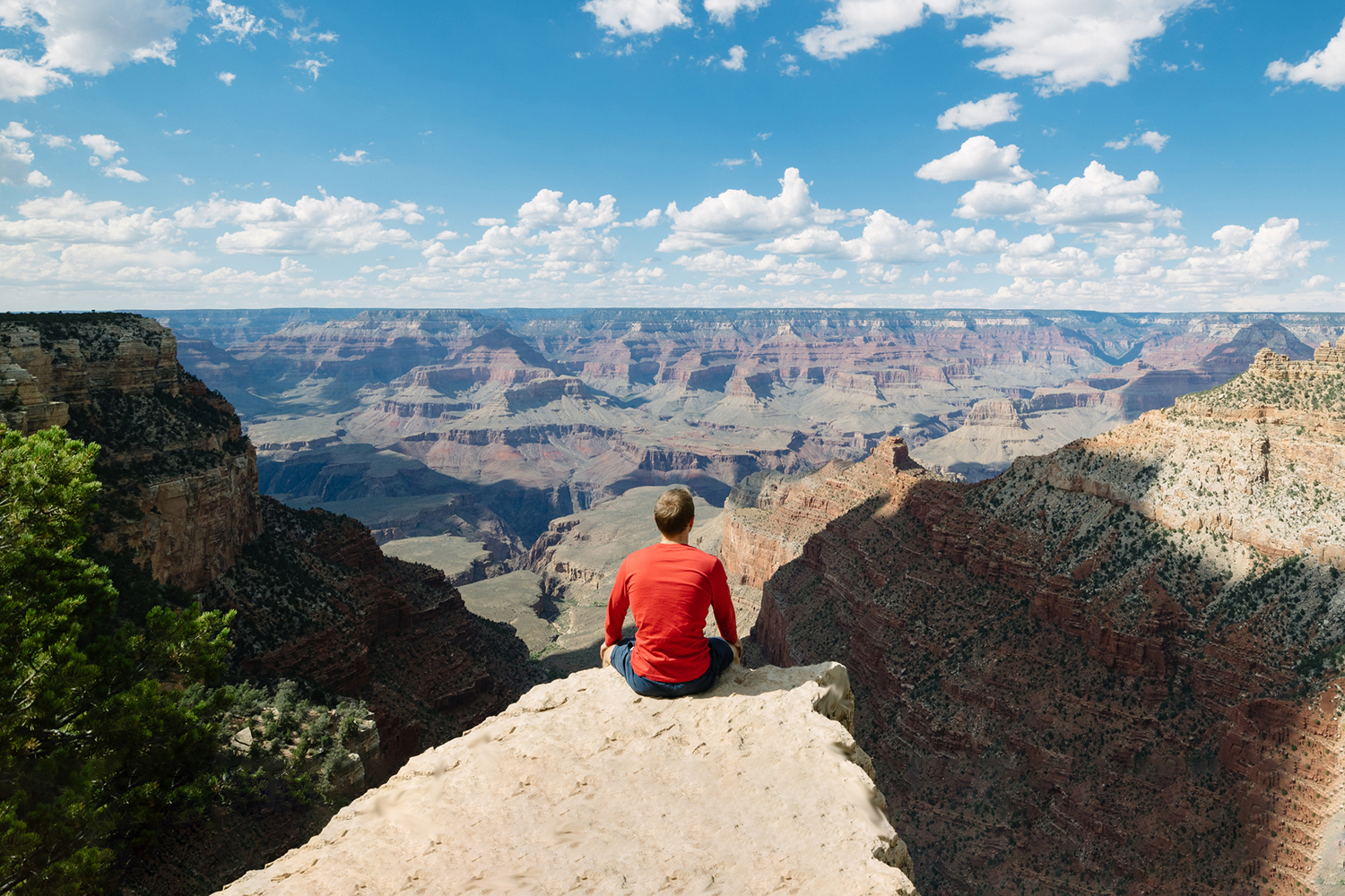 Man sits perched on the rim of epic canyon.